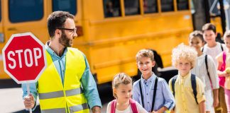 handsome traffic guard crossing road with pupils in front of school bus